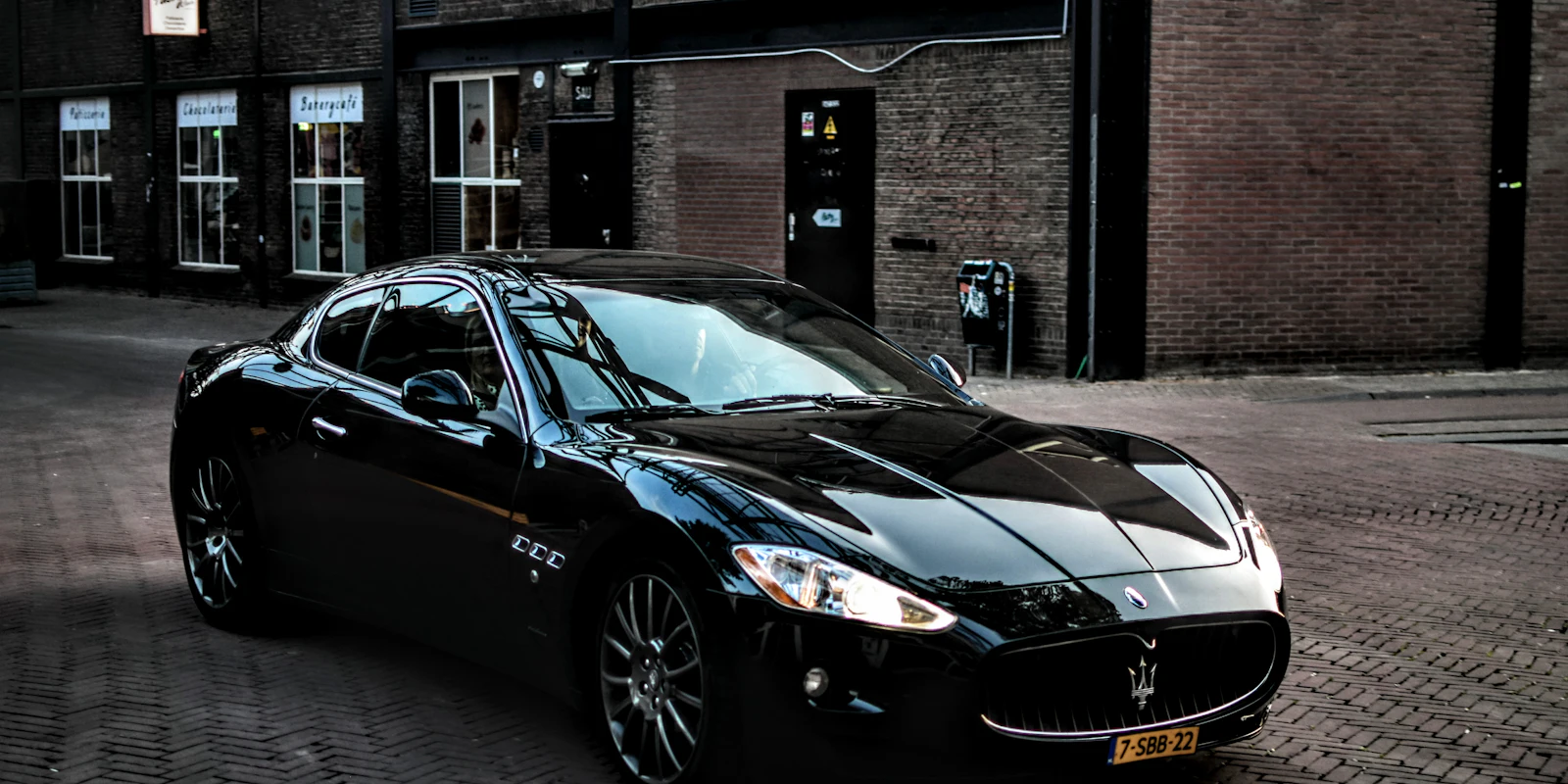 Black Maserati GranTurismo parked by a brick building